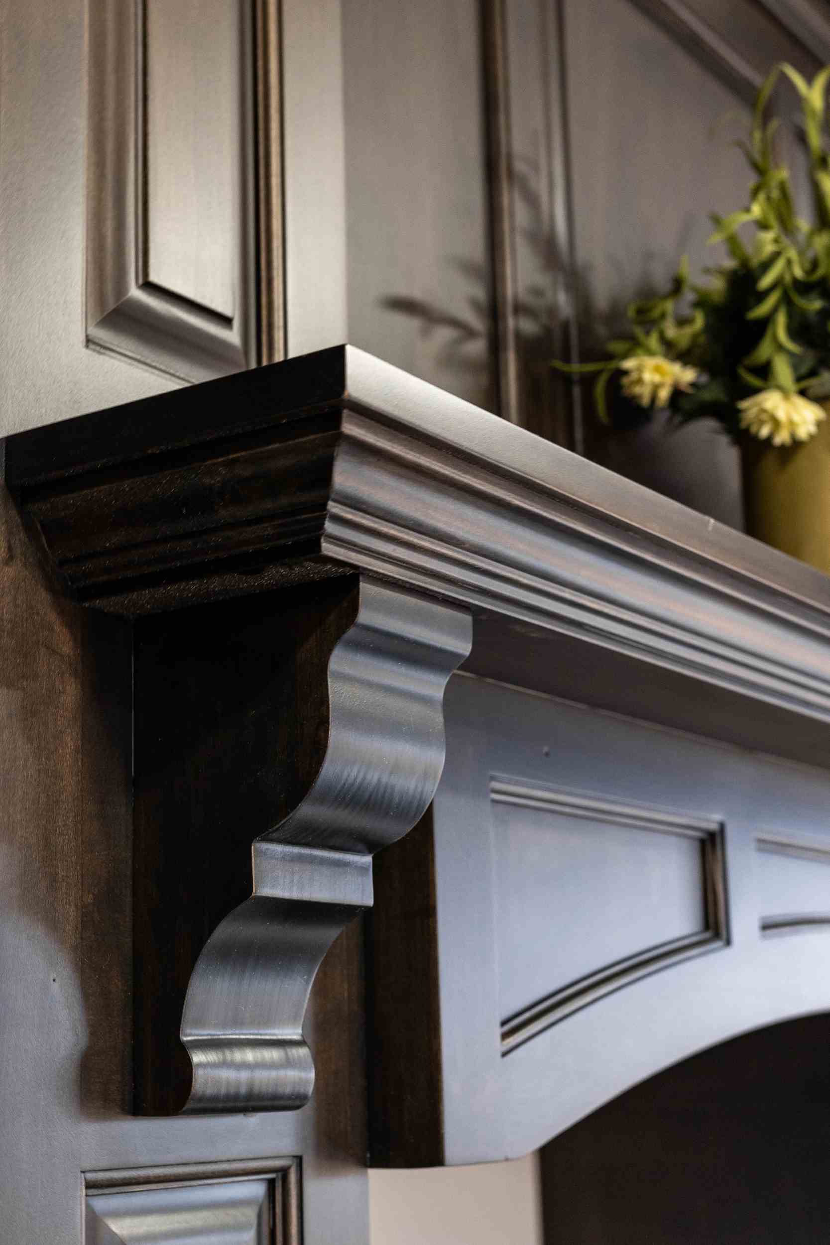 Close-up of a dark wooden decorative corbel supporting a mantel shelf with intricate molding and panel details.