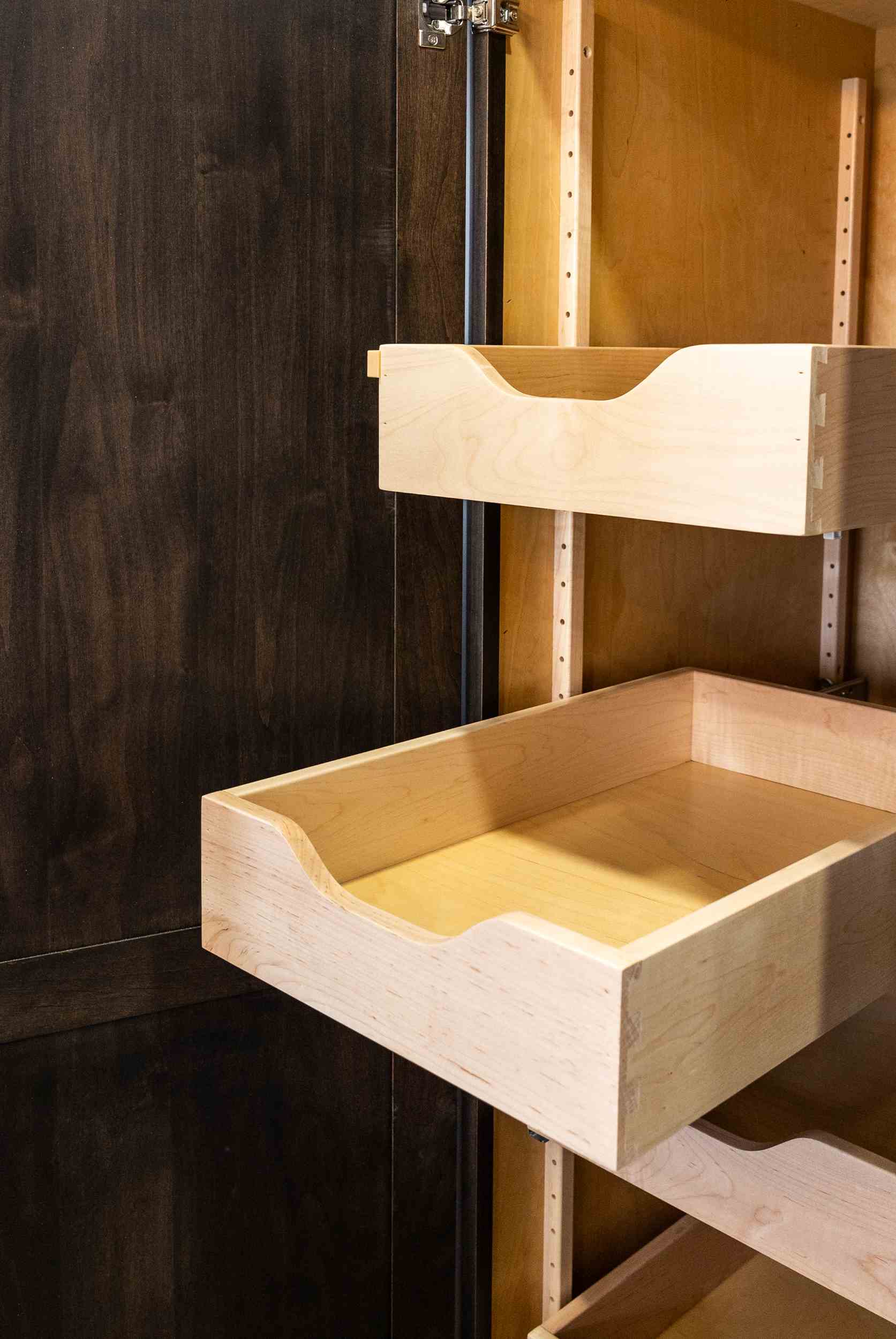 Light wooden empty sliding drawers inside a wooden cabinet with dark wooden door.