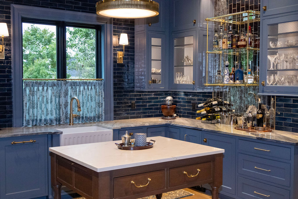 Modern kitchen with white marble countertop island, gray upholstered bar stools, dark wood cabinets, wall-mounted flat-screen TV, and wine cooler.