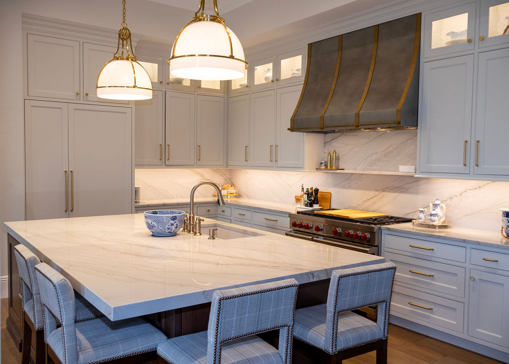 Modern kitchen with white marble countertop island, gray upholstered bar stools, dark wood cabinets, wall-mounted flat-screen TV, and wine cooler.