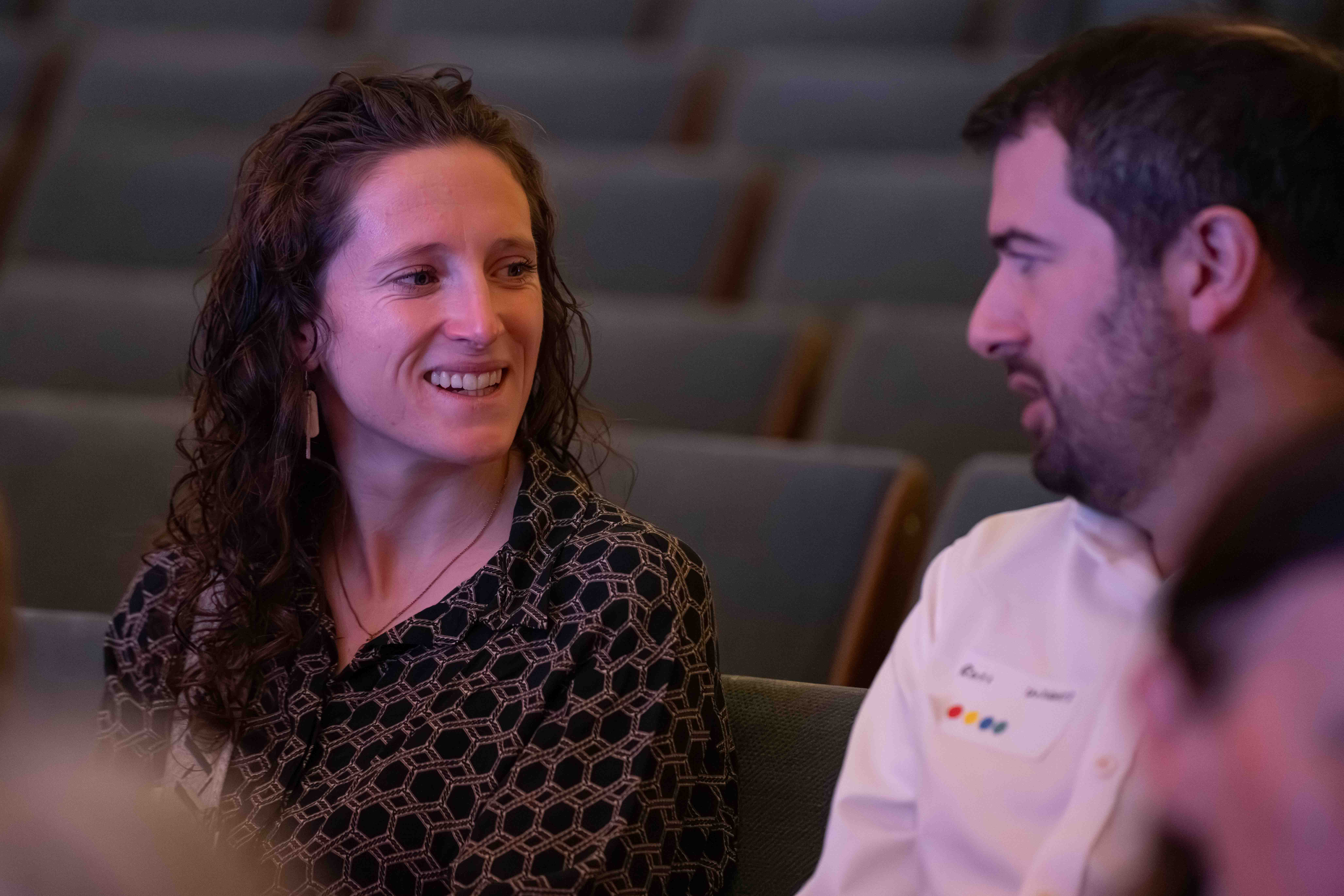 Two people sitting and conversing in a lecture hall with empty seats in the background.