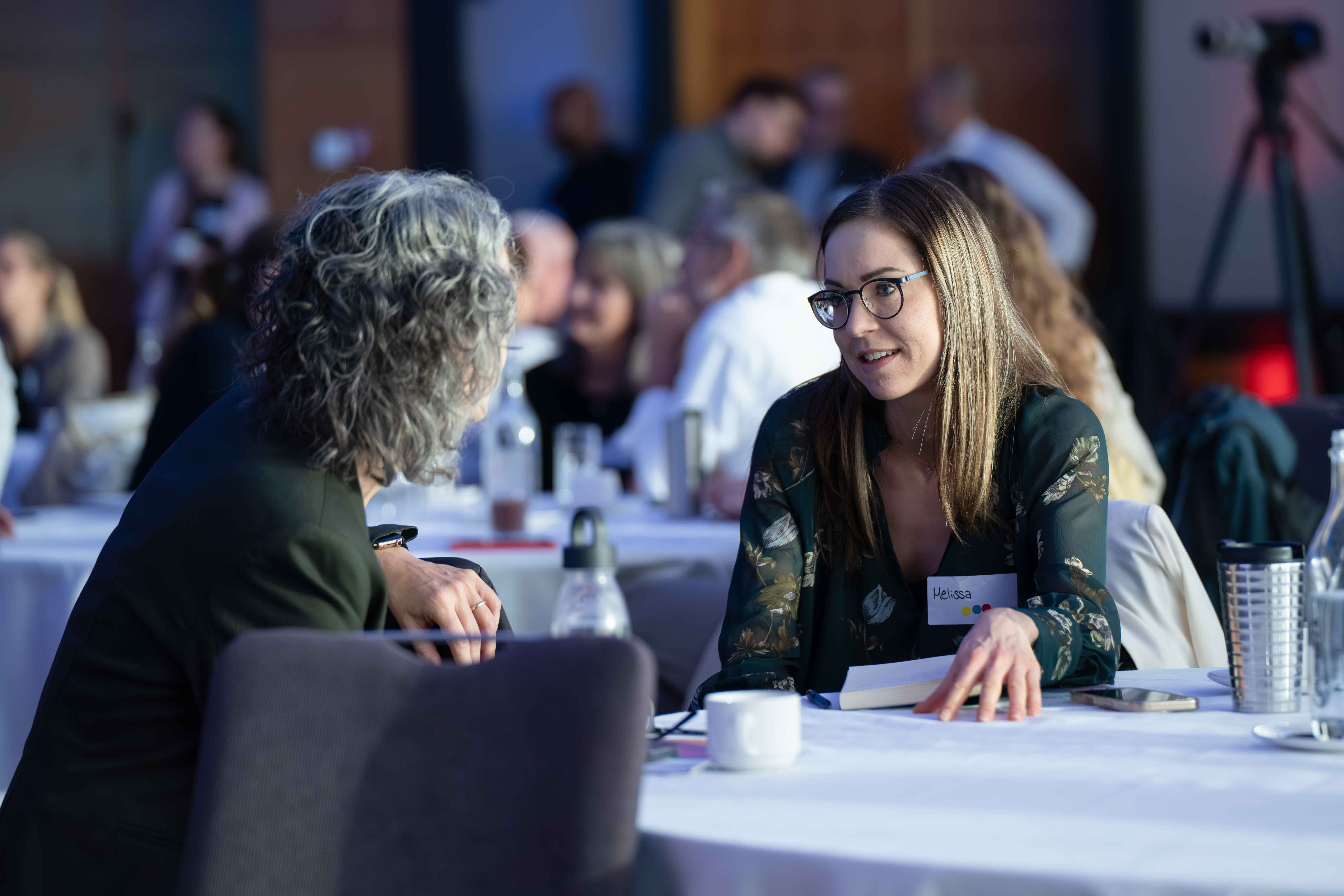Two women having a focused conversation at a round table during a conference or meeting.