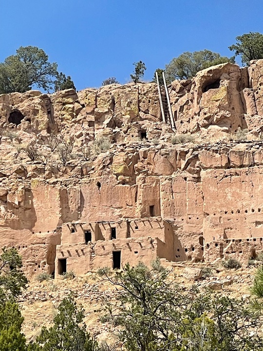 Ancient cliff dwellings at Bandelier National Monument in New Mexico, with ladders leading to carved cave homes.