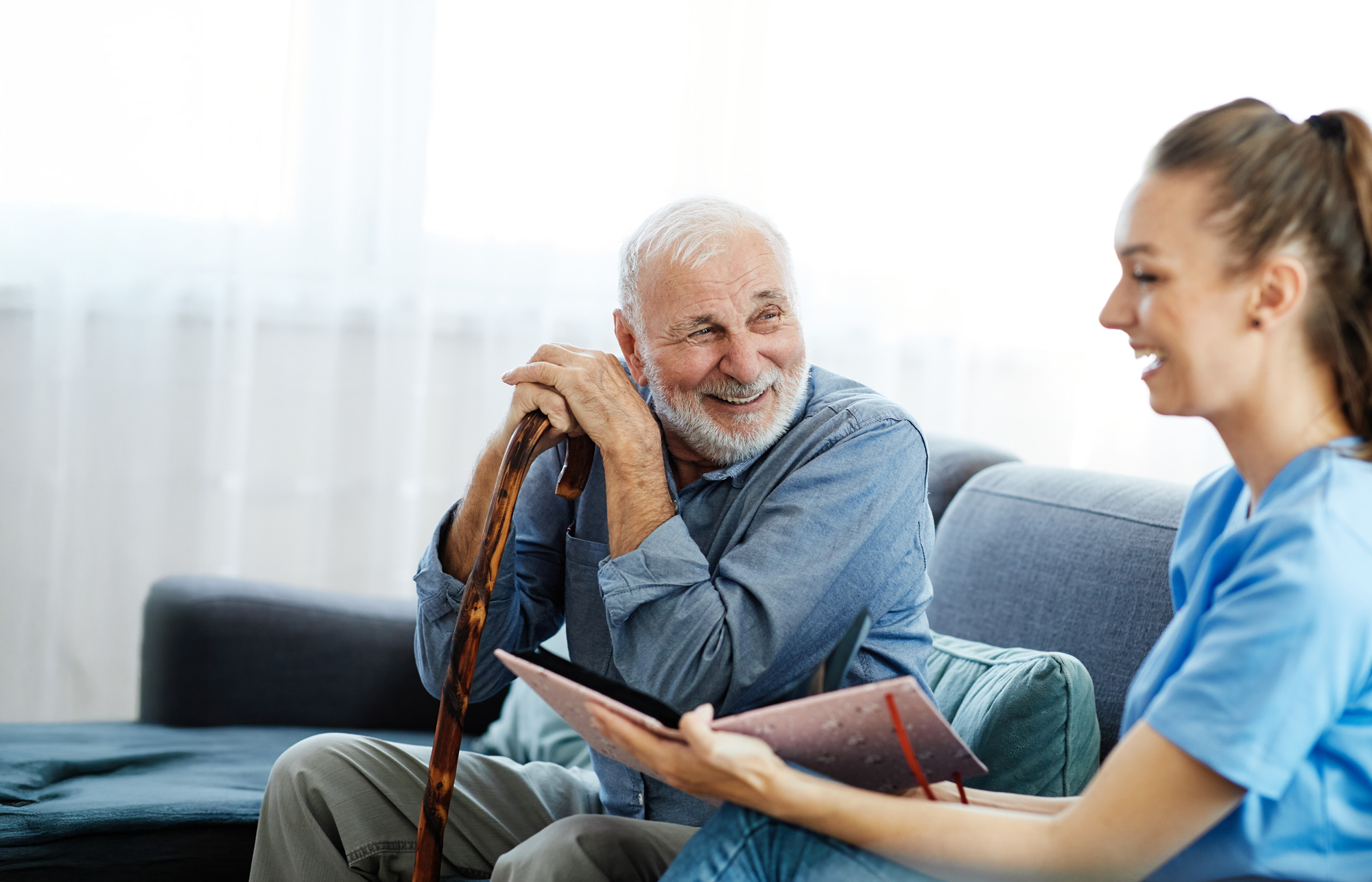 Caregiver sitting on couch with smiling elderly man