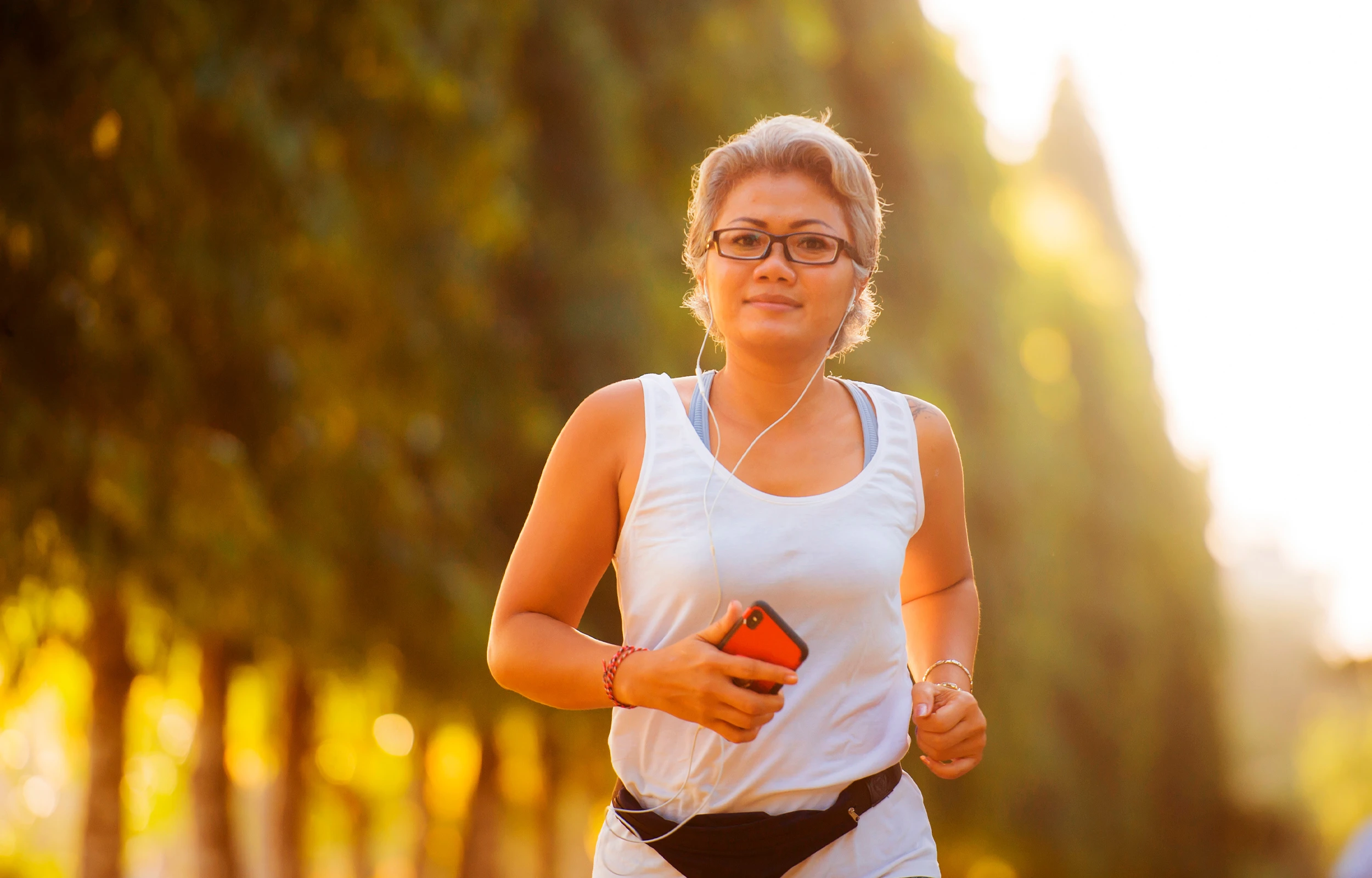 Smiling man in white t-shirt preparing a fresh green salad in a bright kitchen with various vegetables and bread on the counter.