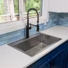 Modern kitchen sink with a black spring coil faucet set into a white countertop with blue subway tile backsplash and blue cabinets.