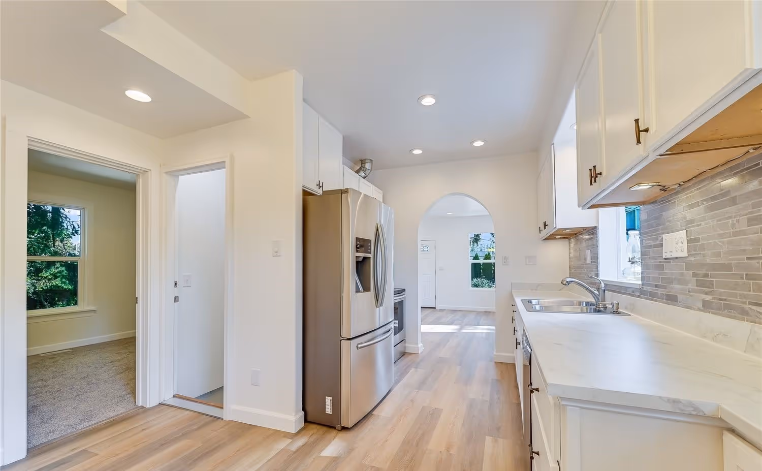 Modern kitchen with white cabinets, stainless steel refrigerator, marble countertops, and light wood flooring.