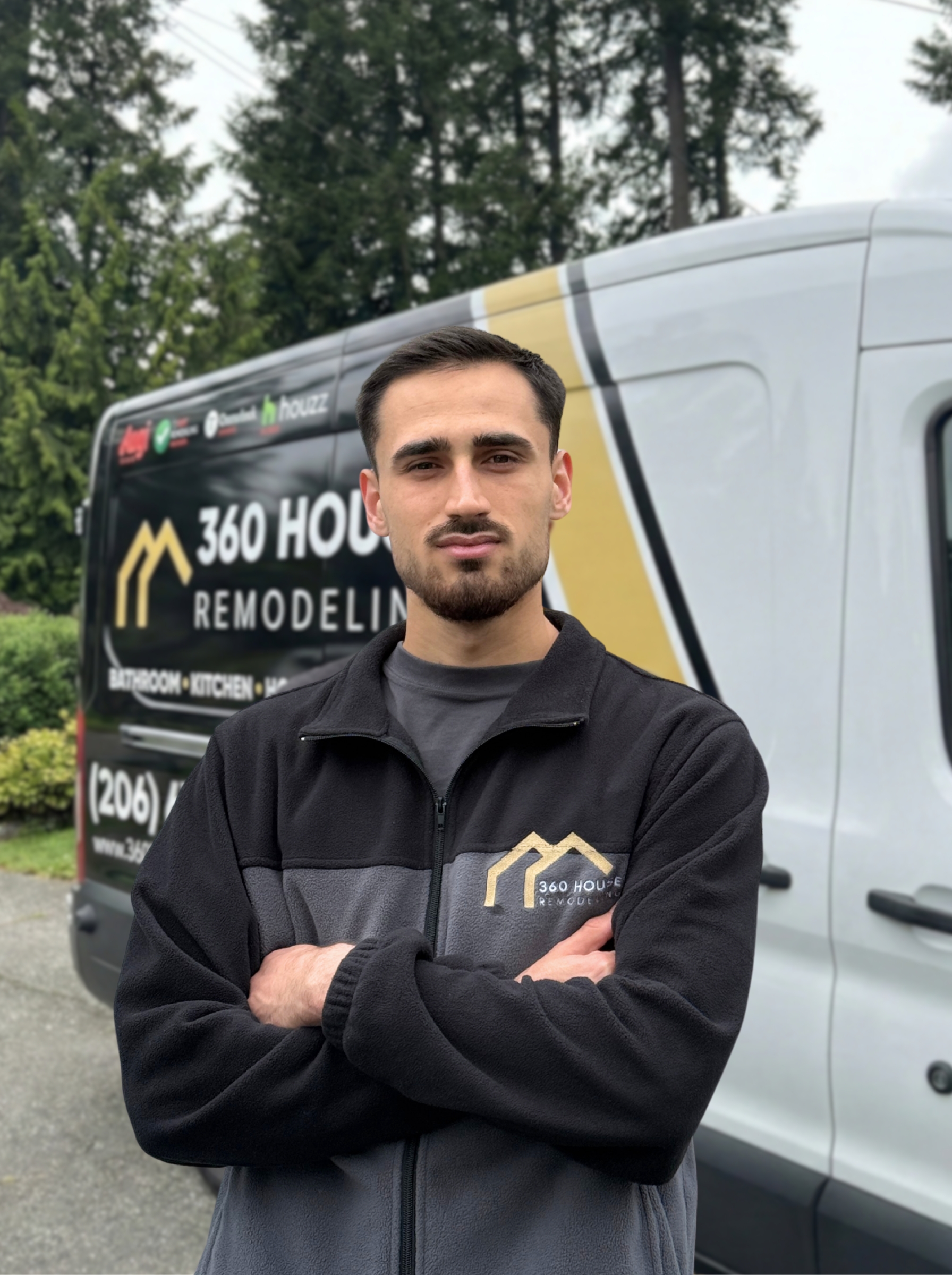 Man with crossed arms wearing a 360 House Remodeling jacket standing in front of a company van with remodeling branding.
