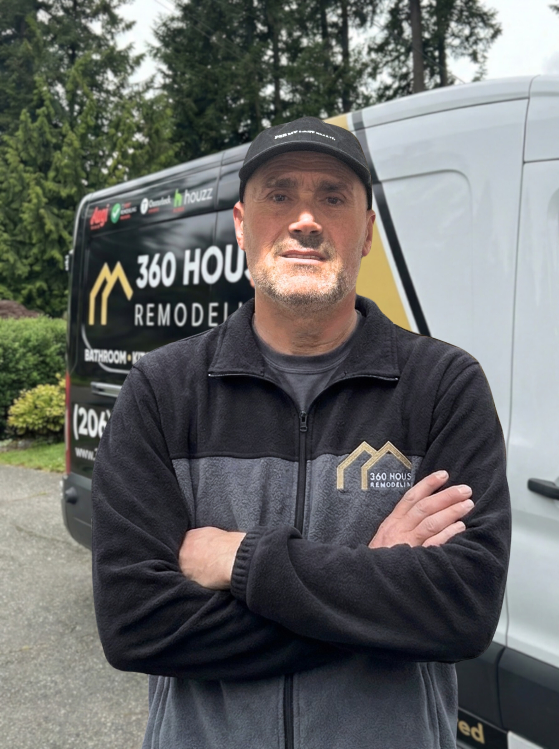 Man wearing a black and gray 360 House Remodeling jacket and black cap, standing with arms crossed in front of a company van.