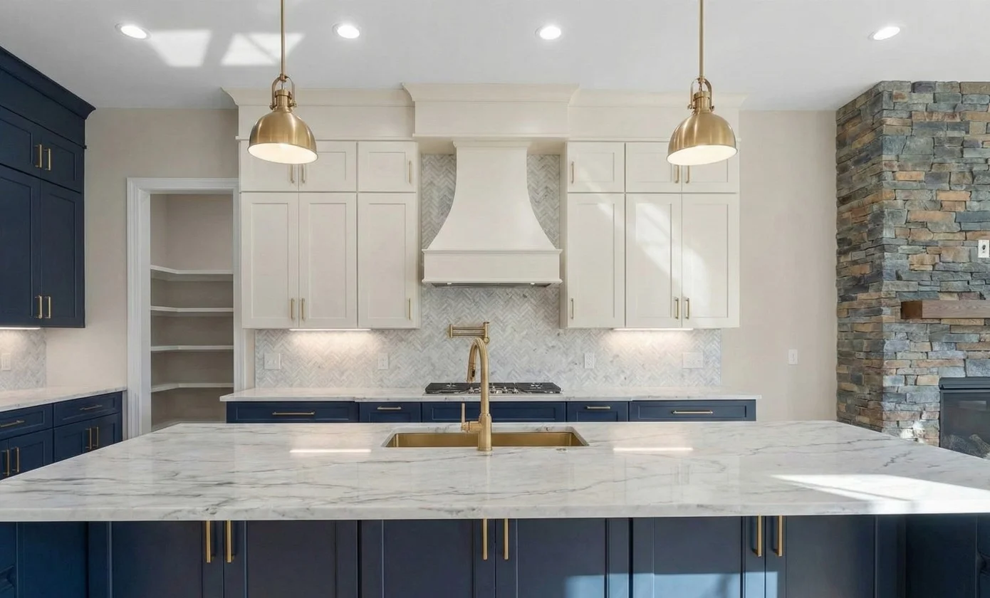Modern kitchen with blue lower cabinets, white upper cabinets, marble island countertop, brass fixtures, and stone accent wall.