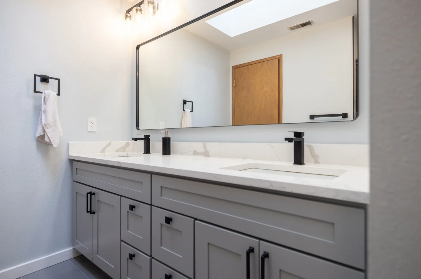 Modern bathroom vanity with gray cabinets, white marble countertop, dual black faucets, and a large rectangular mirror above.