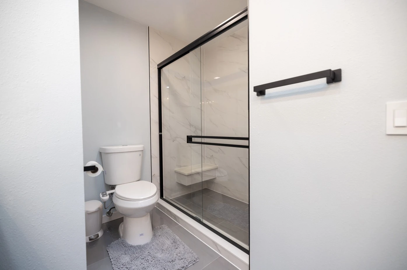 Modern white bathroom vanity with black hardware, rectangular mirror, and light fixture above on gray tiled floor.