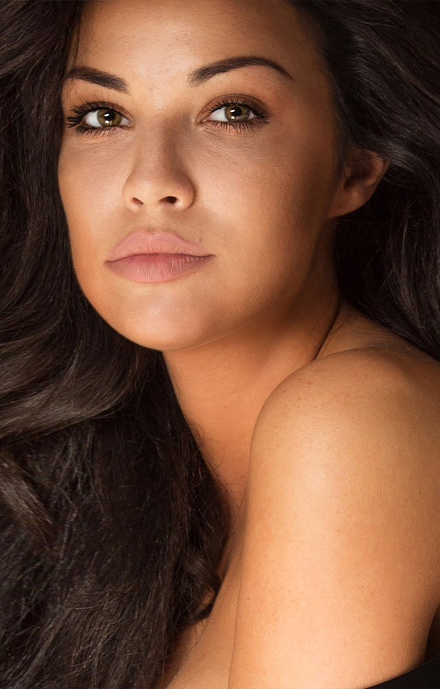 Close-up of a woman with long dark hair, natural makeup, and bare shoulder.