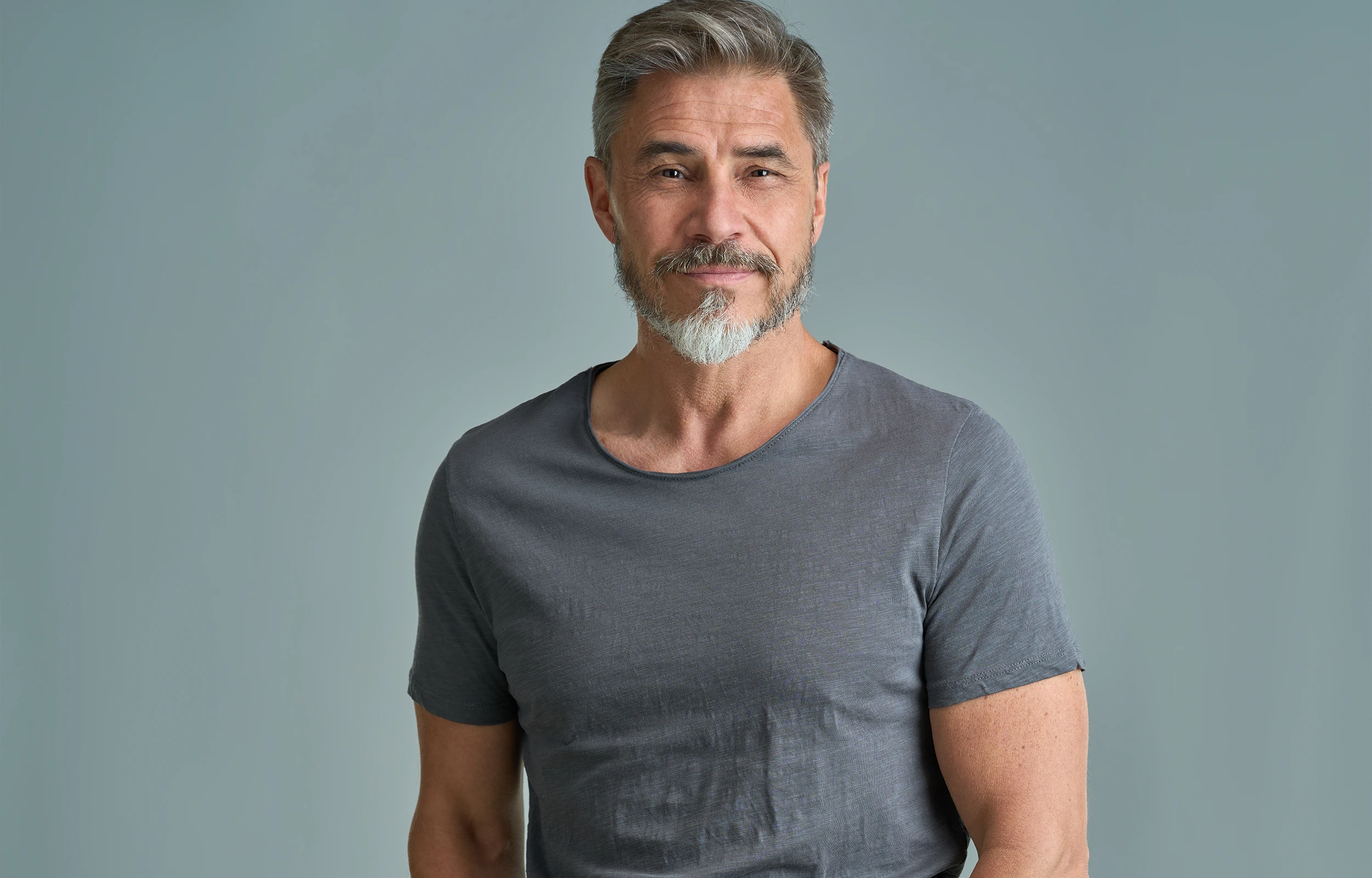 Middle-aged man with gray hair and a two-tone beard wearing a gray t-shirt against a plain background.