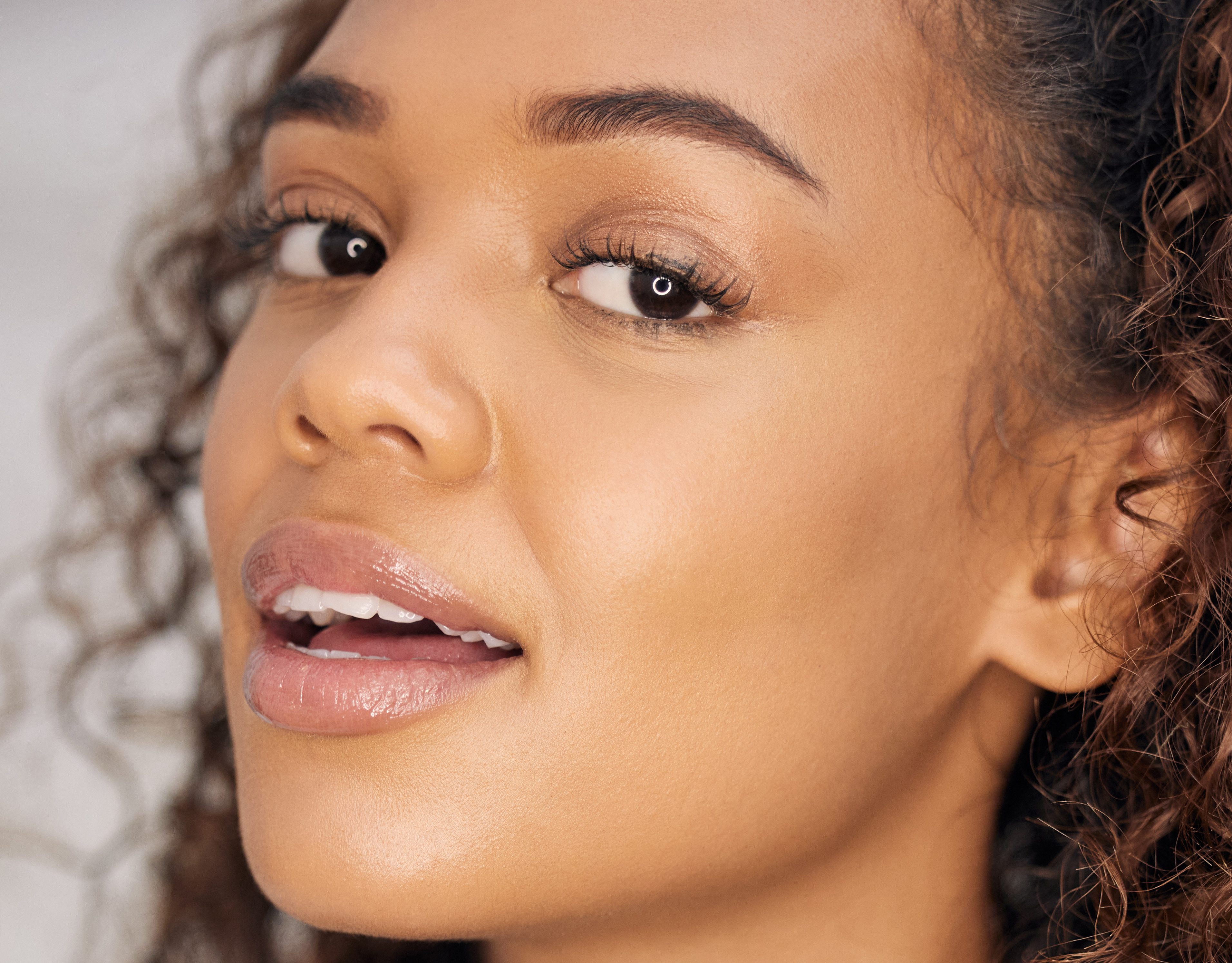Close-up of a woman's face with curly hair, glossy lips, and natural makeup.