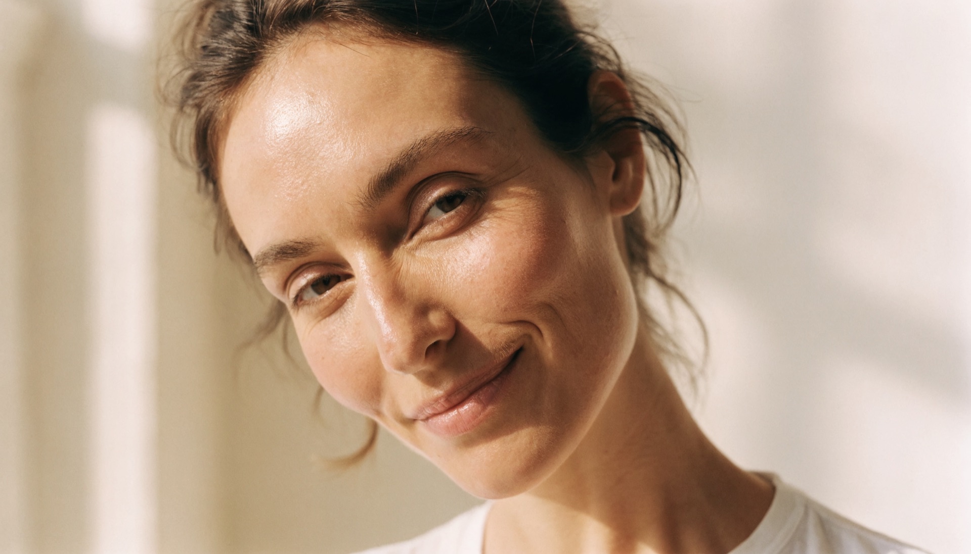 Woman in her late twenties with bare natural skin and a soft smile showing natural expression lines around the eyes