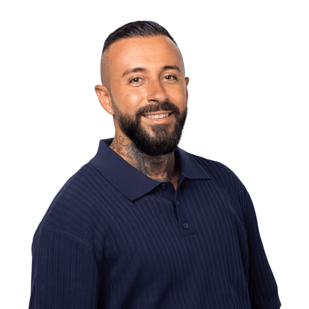 Mann mit kurzem, dunklem Haar, Vollbart und Hals-Tattoo trägt ein dunkelblaues Poloshirt und lächelt freundlich.