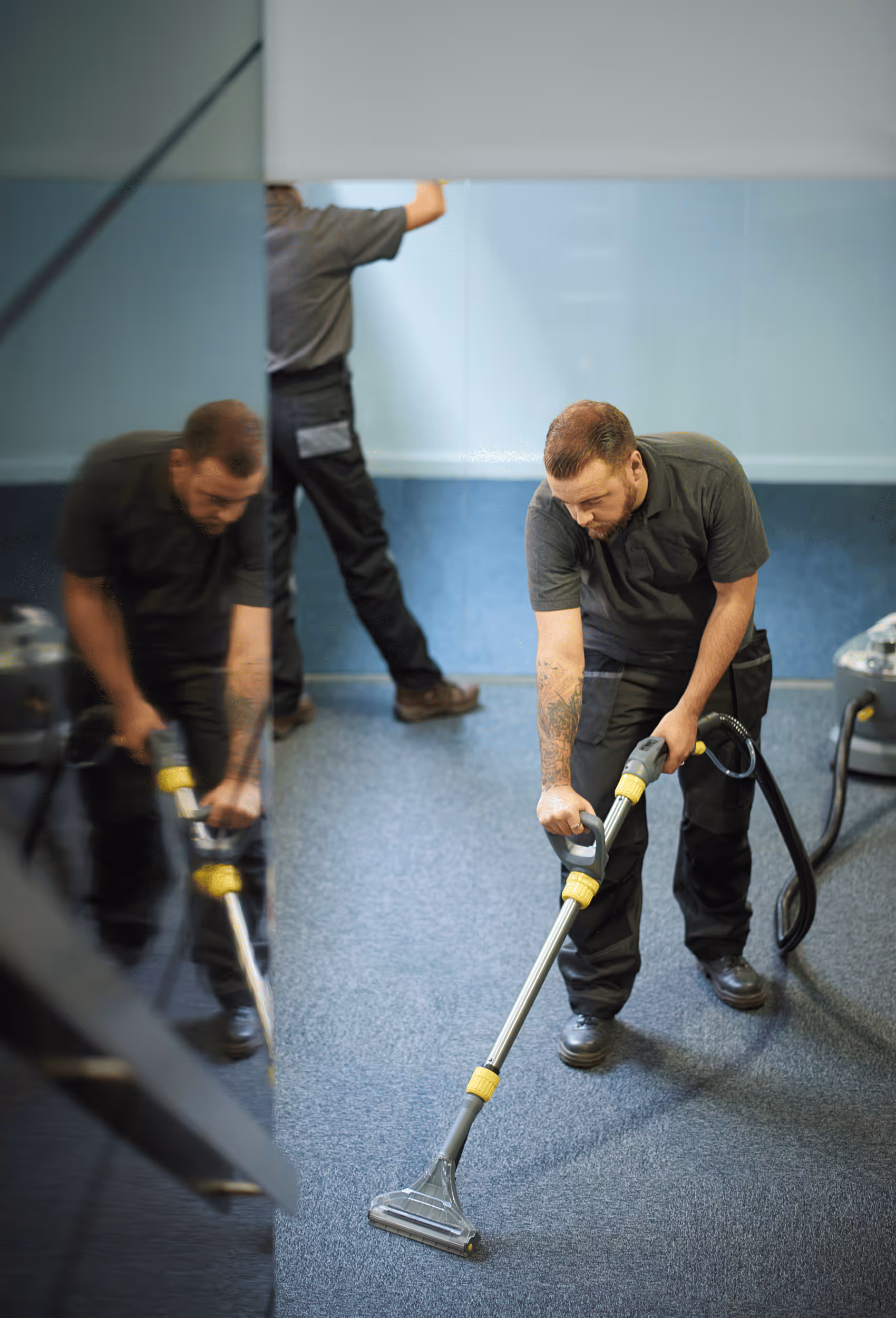 Ein Mann reinigt mit einem industriellen Staubsauger einen blauen Teppichboden in einem Büro.