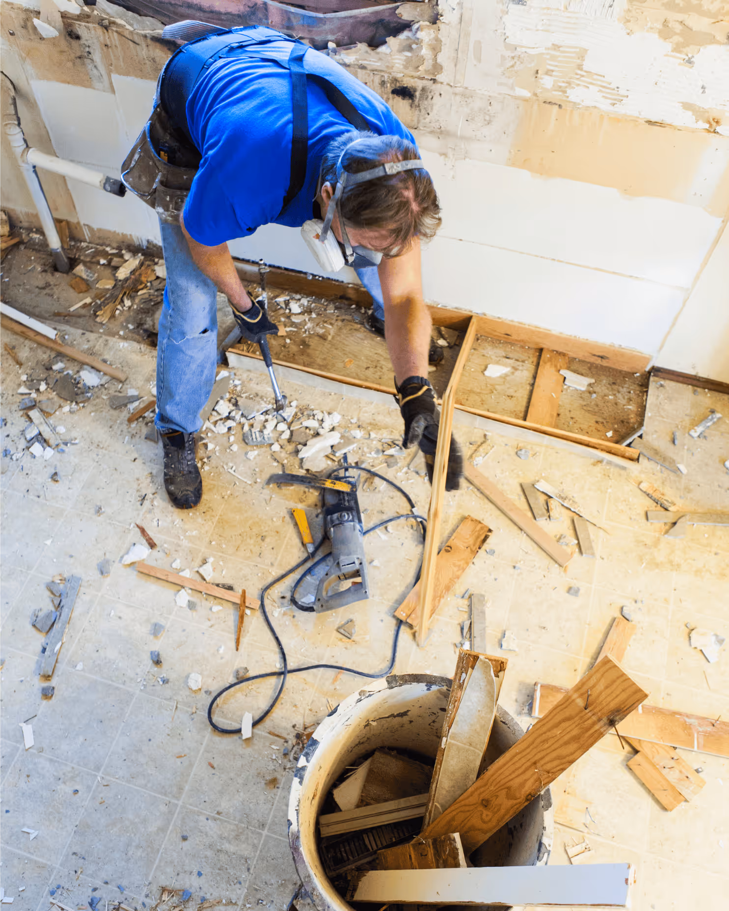 Handwerker mit blauem Hemd und Atemmaske entfernt alte Holzteile bei einer Renovierung.