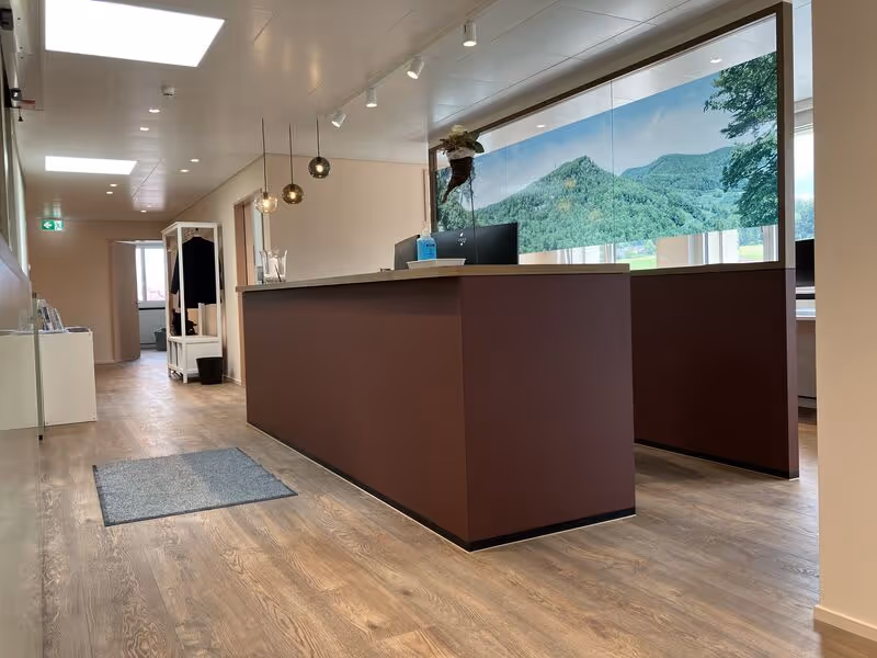 Rezeption mit braunem Tresen in einem hellen Raum mit Holzboden und einem grossen Fenster mit Bergsicht.