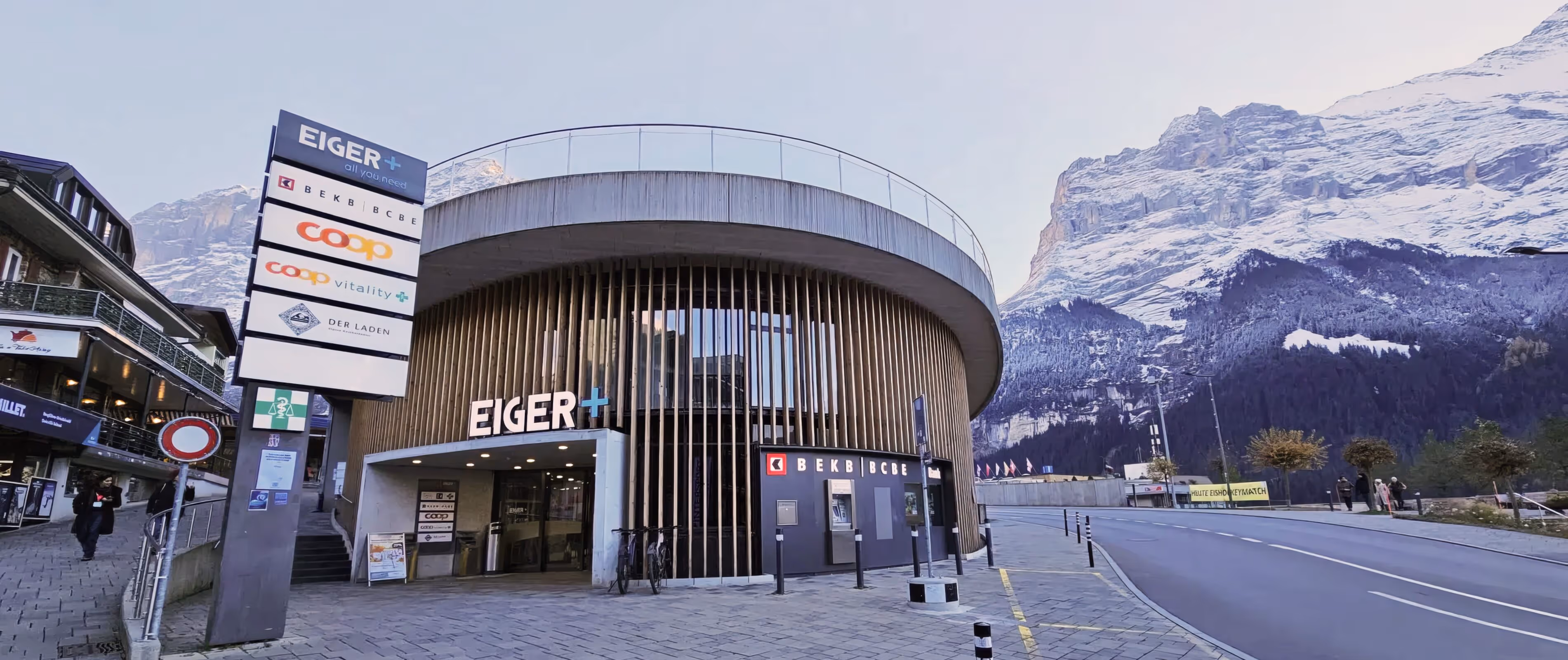 Rundes modernes Einkaufszentrum Eiger mit Geschäften und Banken vor schneebedecktem Berg in Grindelwald.