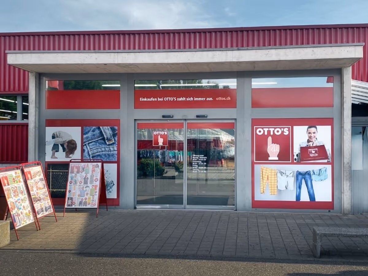 Eingang eines OTTO'S Geschäftes mit roten Werbeplakaten und automatischen Glastüren.