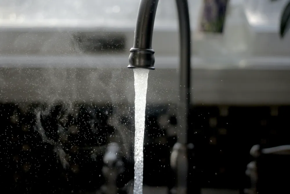 Close-up of hot water flowing from a black kitchen faucet with steam rising.