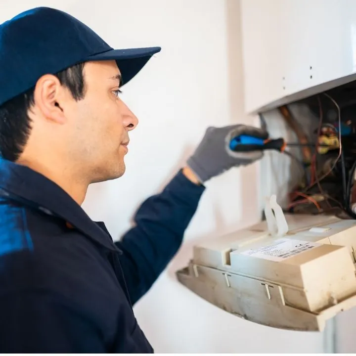 Technician in a navy uniform and cap using a screwdriver to repair an electrical panel.