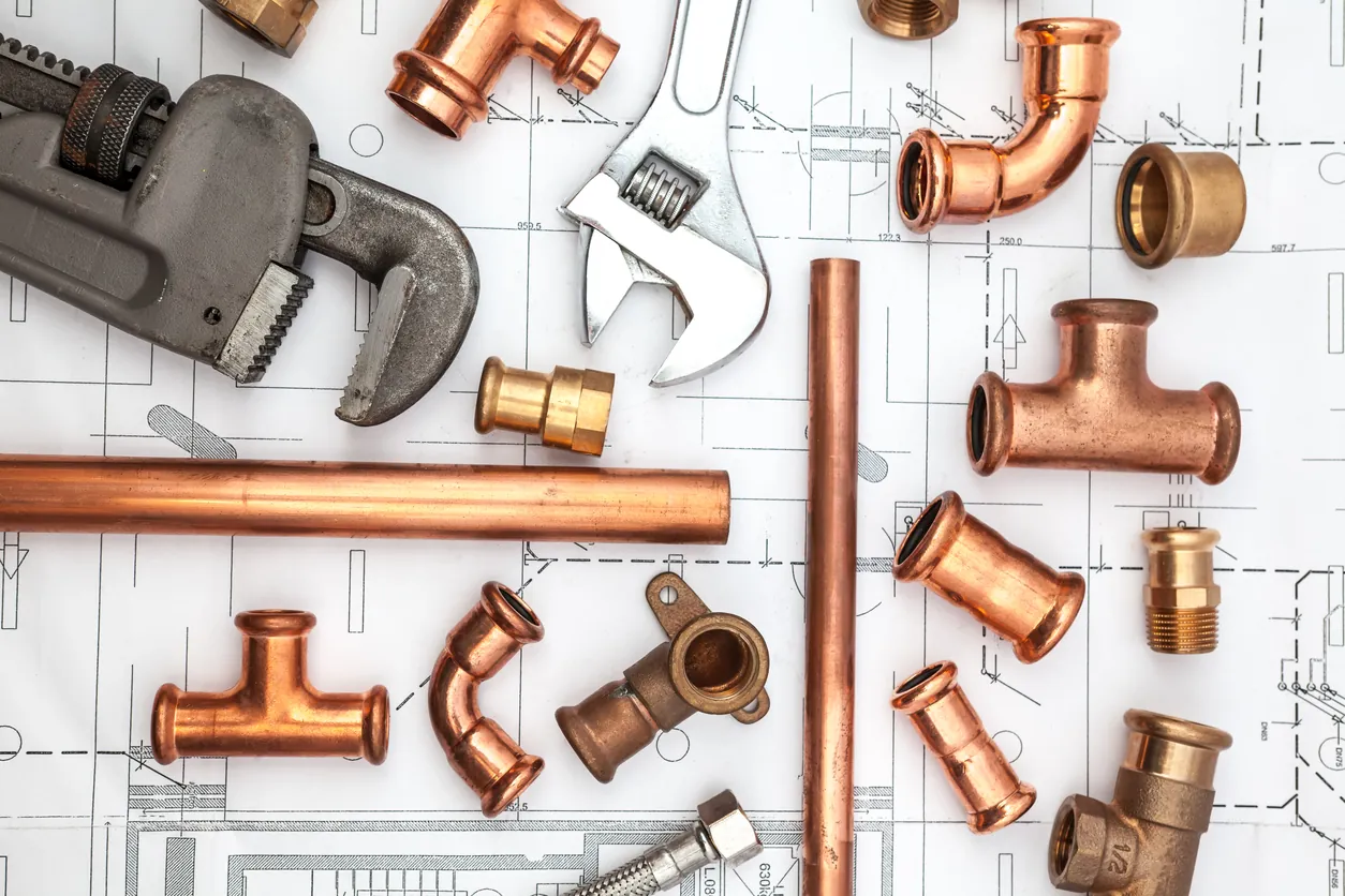 Various copper plumbing pipes, fittings, and wrenches laid out on a technical blueprint.