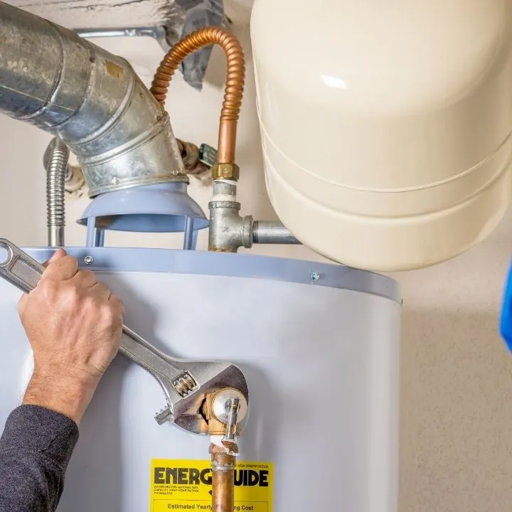 Person using a wrench to adjust plumbing on a water heater with visible pipes and an energy guide label.