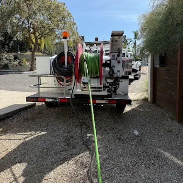 Plumbing truck and drain cleaning machine set up outside a home for sewer maintenance.