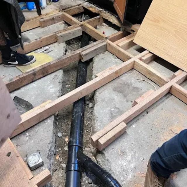 Exposed floor framing with new black drain pipes installed during plumbing renovation.