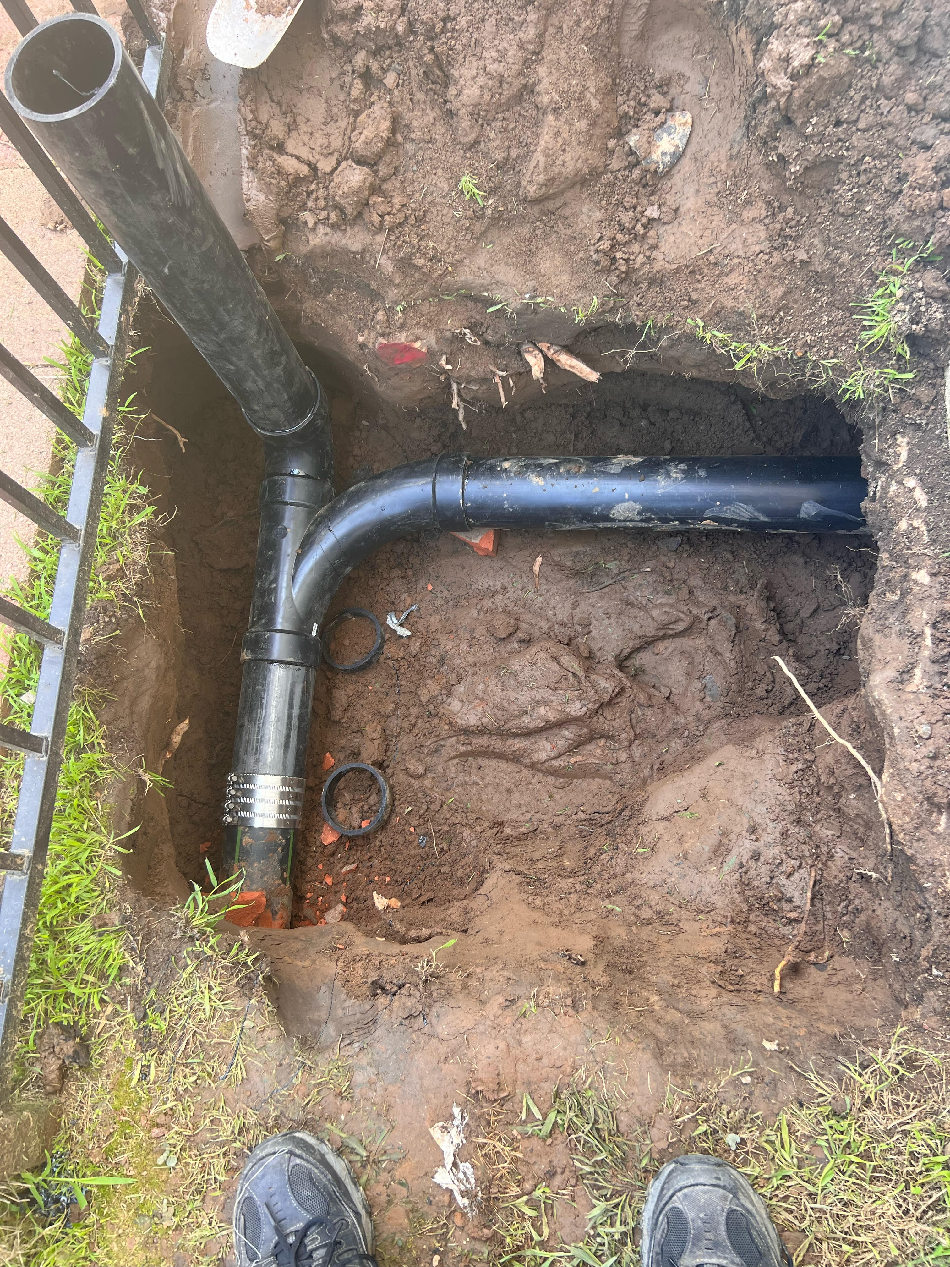 New black ABS sewer pipe installed in an excavated trench during underground plumbing repair.