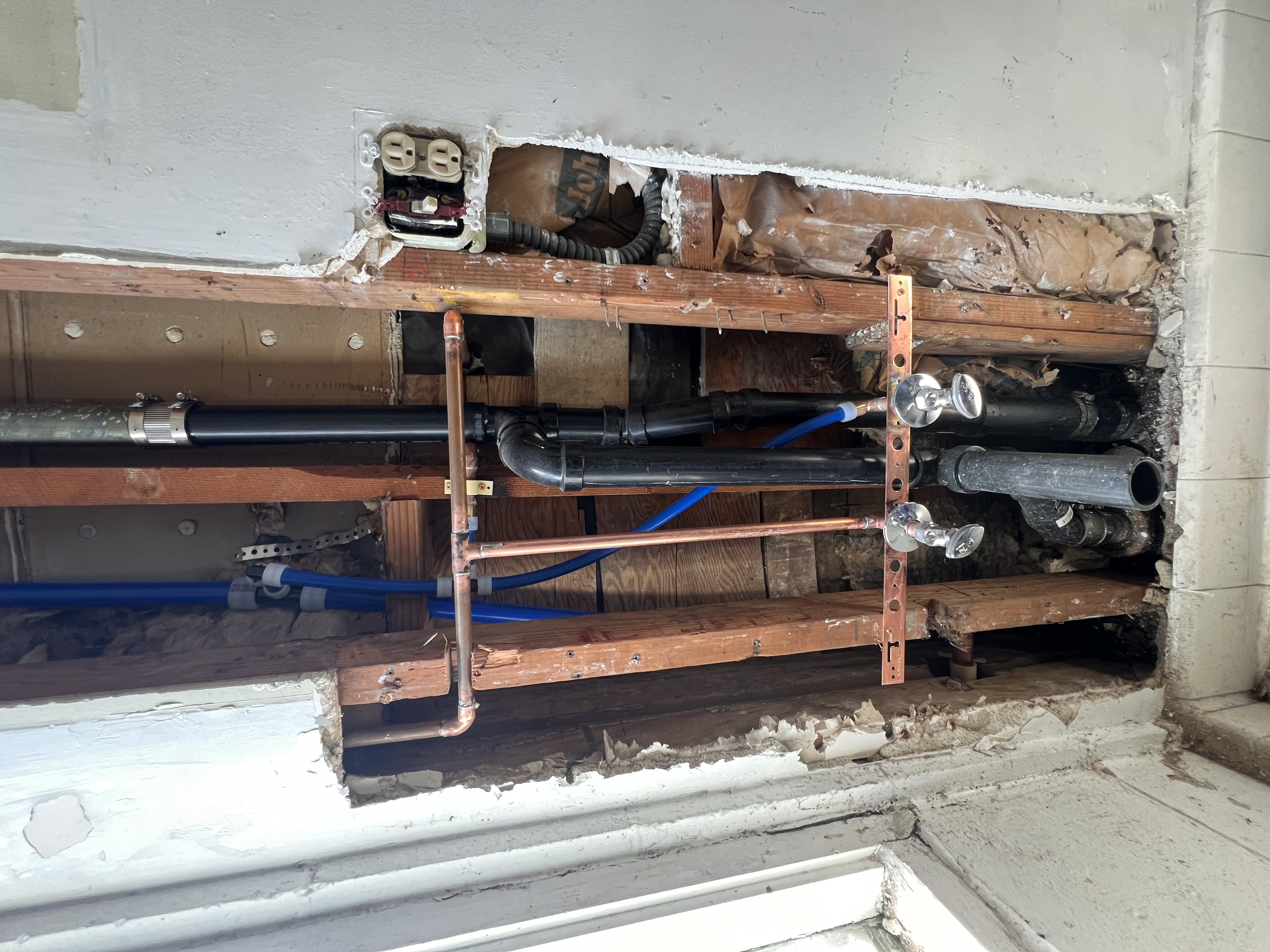 Exposed wall plumbing with copper water lines and black drain pipe during bathroom rough-in installation.
