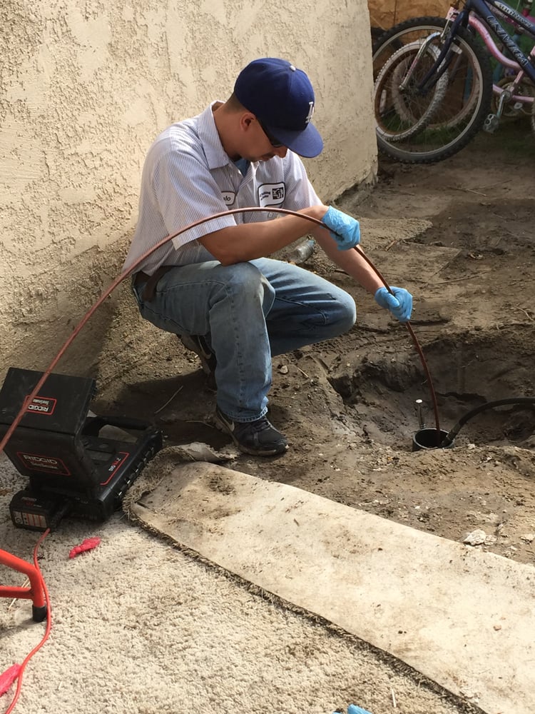 Technician inserting sewer inspection camera into outdoor cleanout for drain diagnostics.