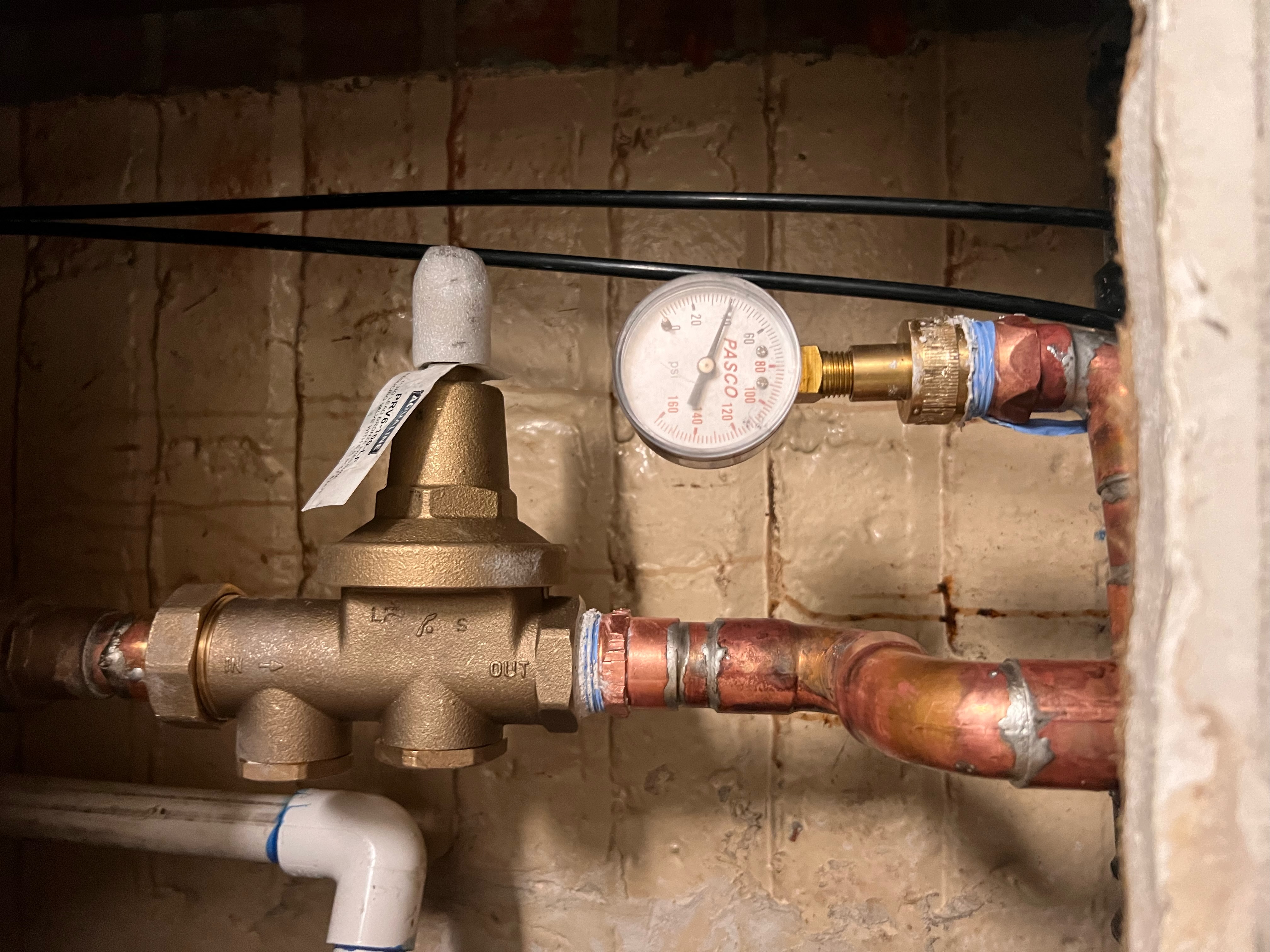 Water pressure regulator and gauge installed on copper plumbing line.