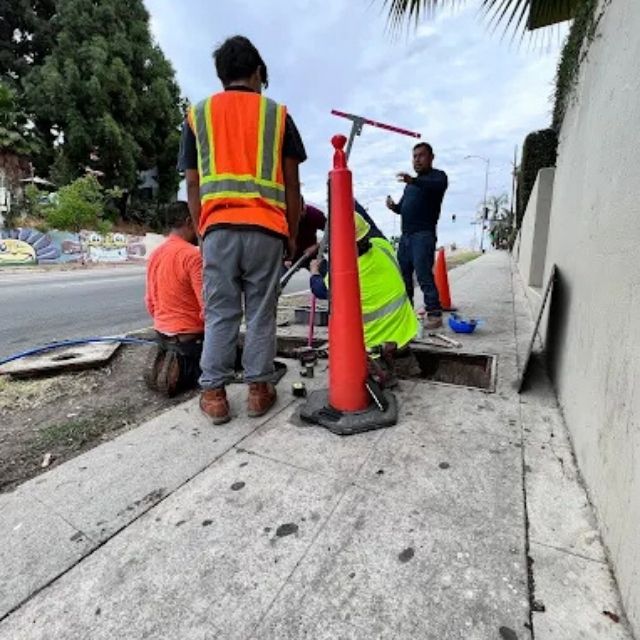 Plumbing crew performing sewer line repair at sidewalk access point.