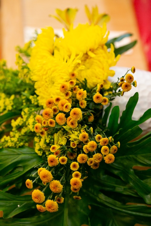 Close-up of a bright yellow flower bouquet with small round blooms and large green leaves.
