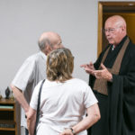 A man in religious attire speaking to two people, one man and one woman, who are listening attentively.