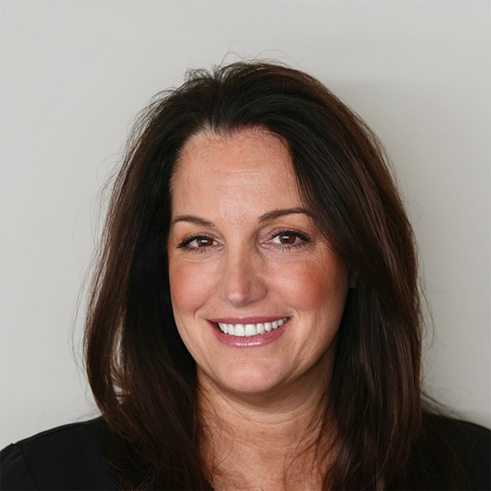 Smiling woman with long dark brown hair wearing a black top against a plain light background.