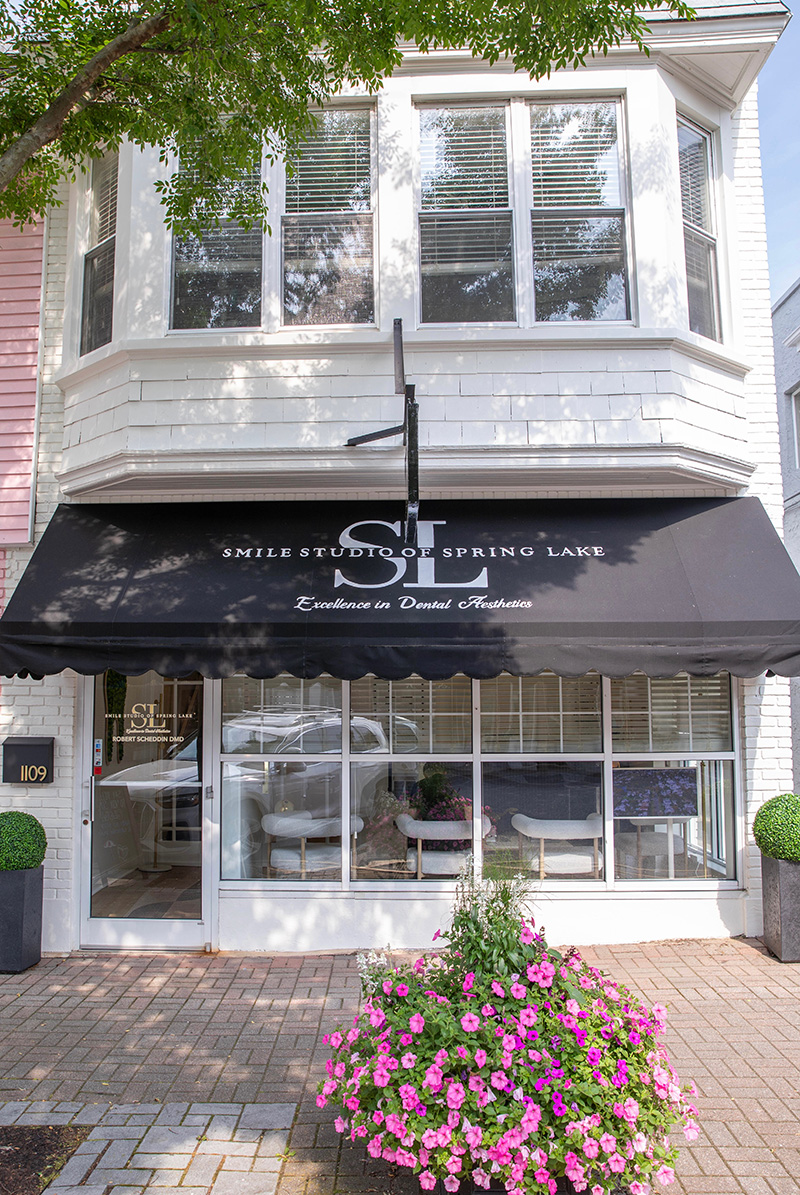Exterior of Smile Studio of Spring Lake dental office with black awning, large windows, and pink flowers in front.