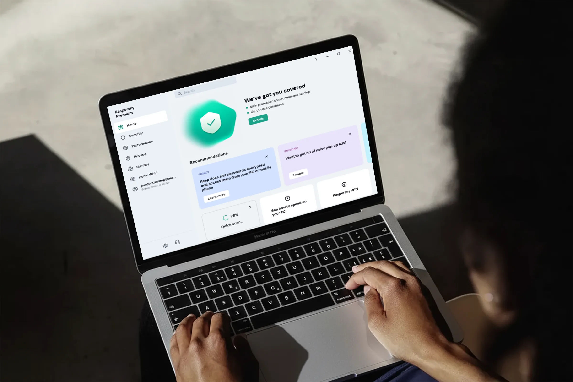 Person using a MacBook Pro laptop displaying Kaspersky Premium antivirus software dashboard with security status and recommendations.