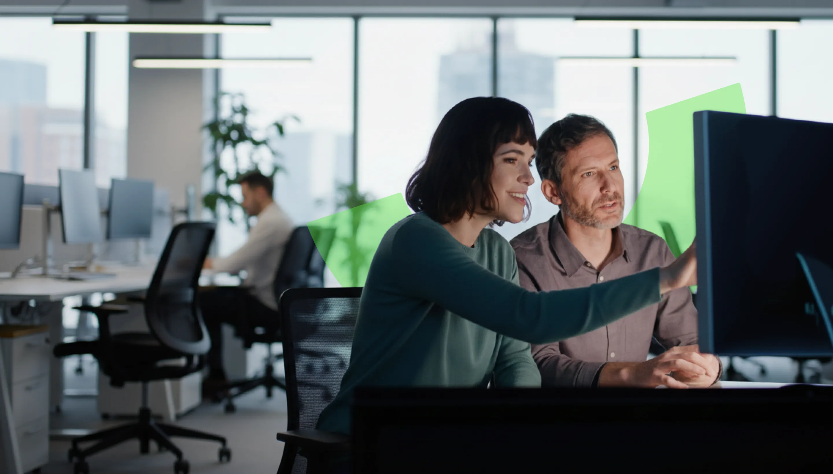 Two colleagues, a woman and a man, working together at a computer in a modern office.