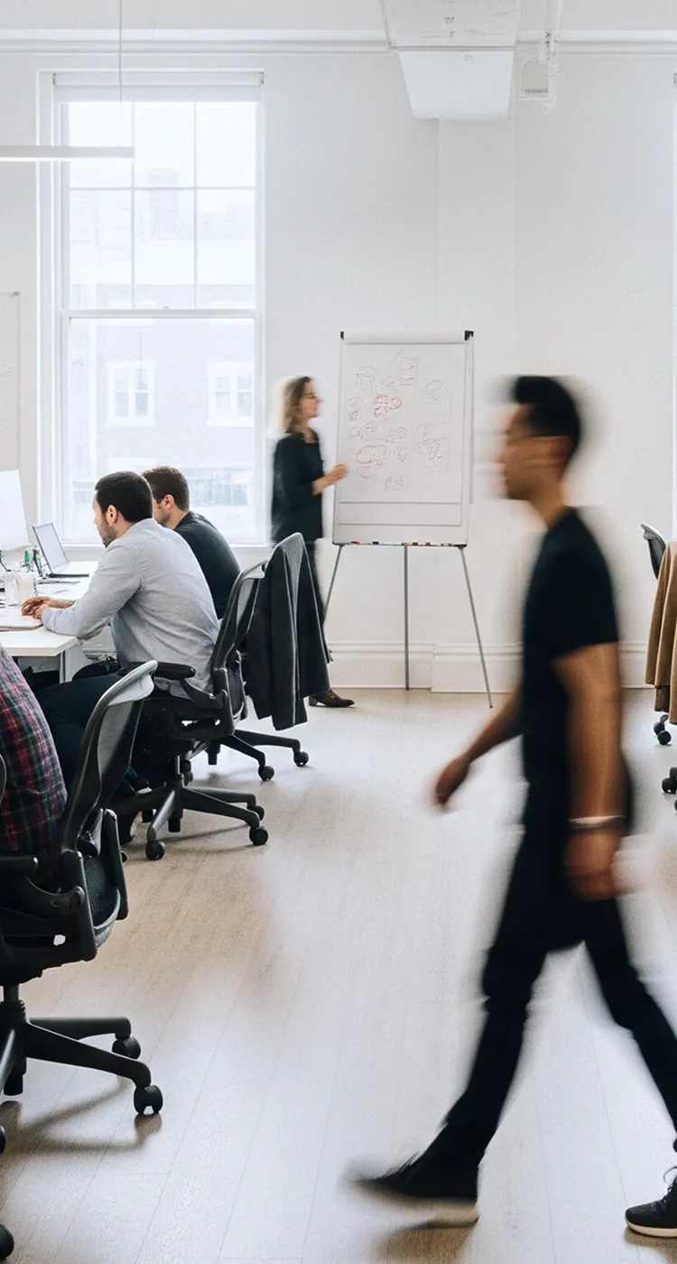 Busy office scene with people working at desks and a woman presenting ideas on a whiteboard.