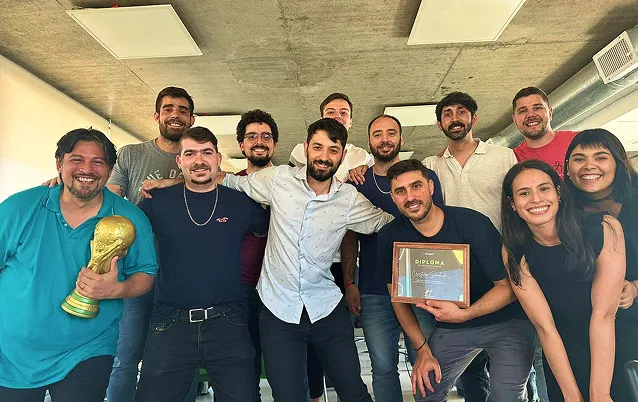 Group of ten smiling people posing indoors, one holding a gold trophy and another showing a diploma plaque.