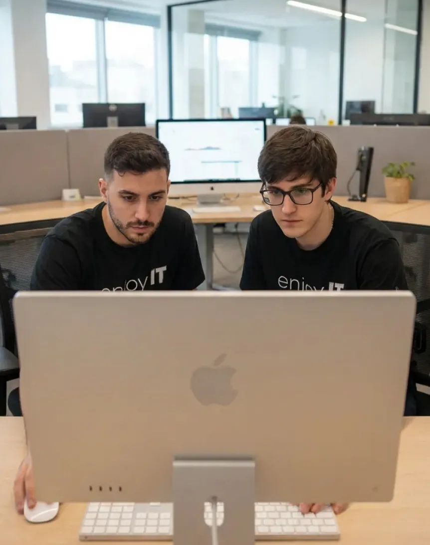Two men focused on a large Apple desktop computer in a modern office setting.