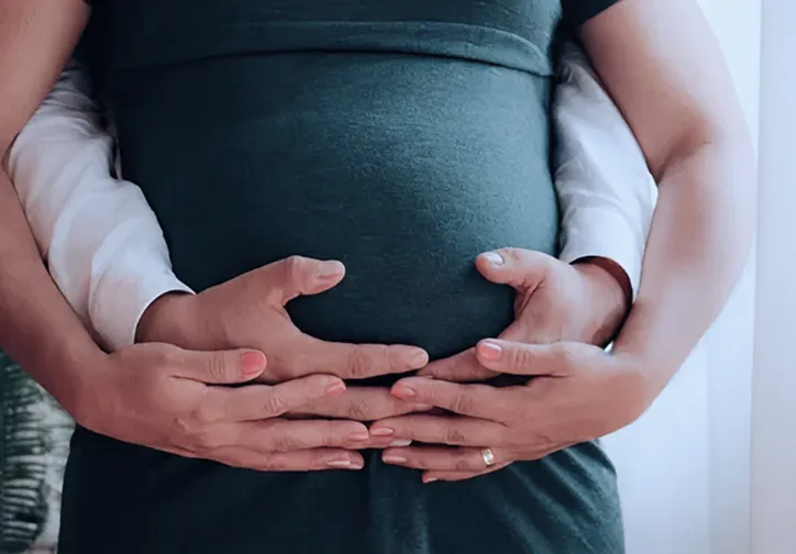 Two people embracing with their hands gently placed on a pregnant belly.