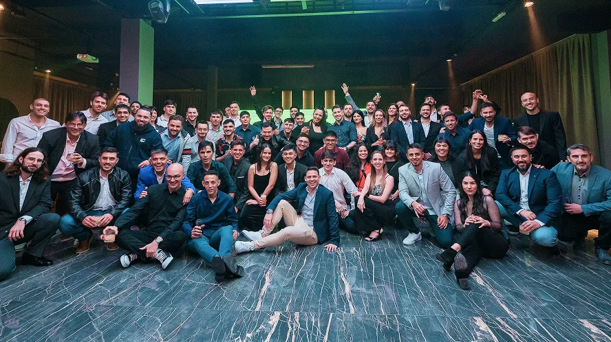 Large group of diverse adults posing and smiling together indoors on a marble floor under bright overhead lights.