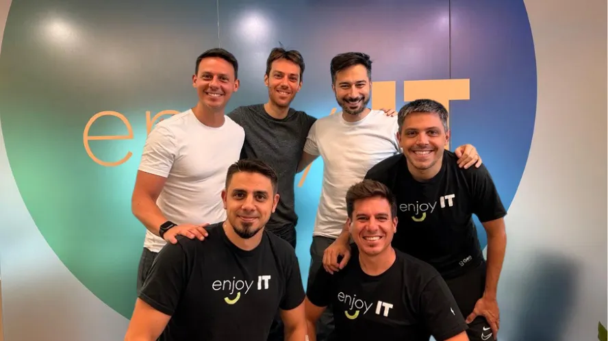 Three smiling men in smart casual and formal attire posing in front of a green Gen IT 10 años juntos banner.