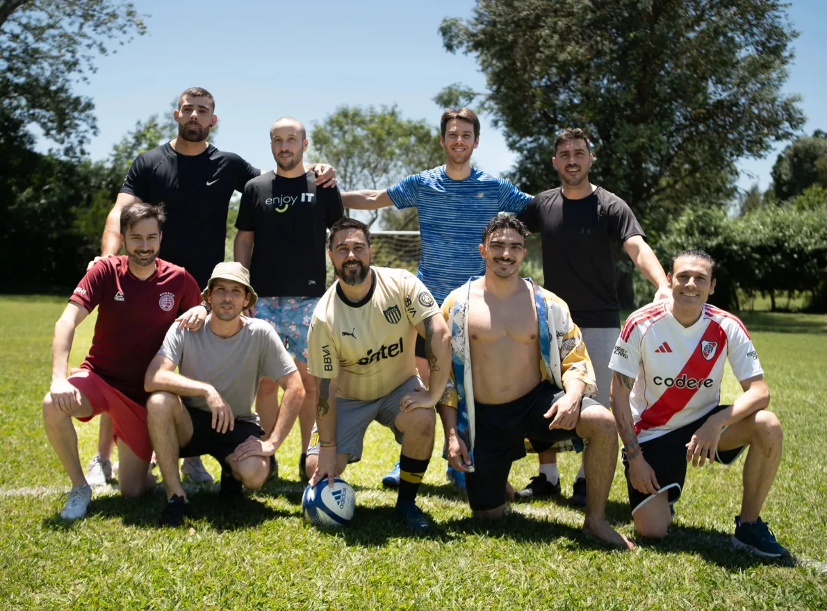 People in a park holding colored smoke flares emitting green and blue smoke, with trees overhead.